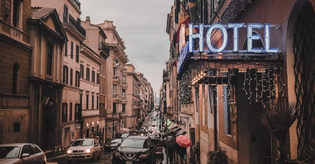 A rainy city street scene at dusk, featuring a glowing neon hotel sign, wet cobblestones, and bustling cars.